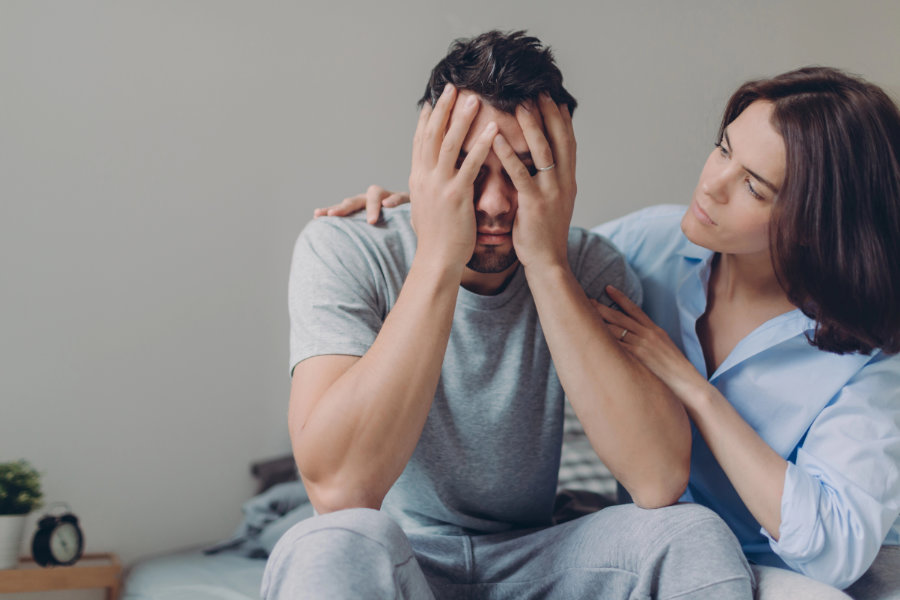 Stressful young man cries from despair, loving mother tries to calm him, pose together at bed against domestic interior, have some problems. Upset husband sees no way out in difficult situation how to support your partner in difficult times - hugs